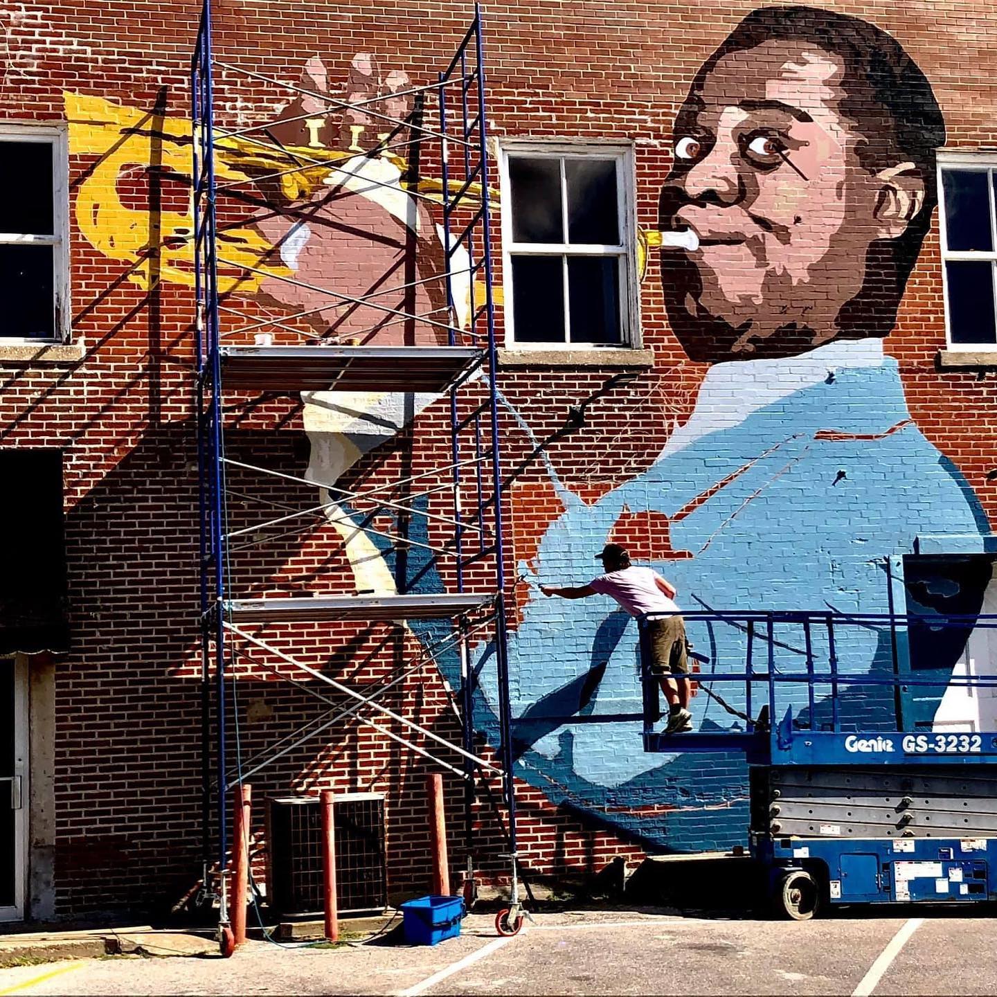 a muralist painting with scaffolding and a scissor jack