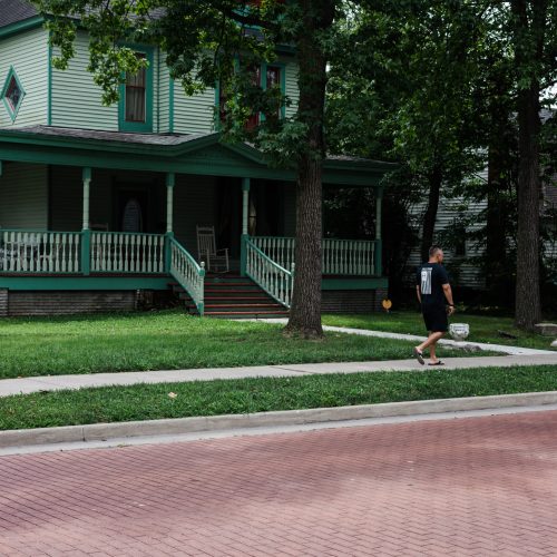 a man walks in front of a historic teal house on a brick road in marion il