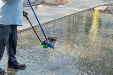 a person uses a broom and dust pan to remove debris from a water way
